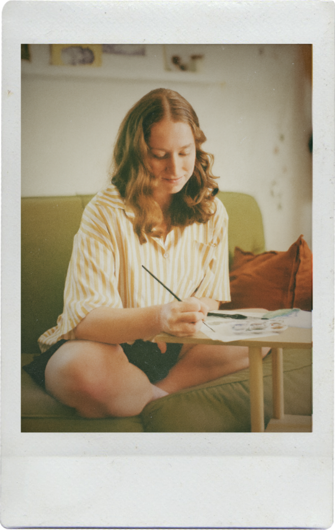 Photo of Amy, watercolor artist behind Fablefern Studio, sitting and painting invitations.